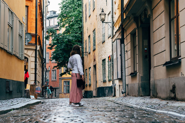 Beautiful young woman is looking back in picturesque narrow street amidst old buildings in stockholm