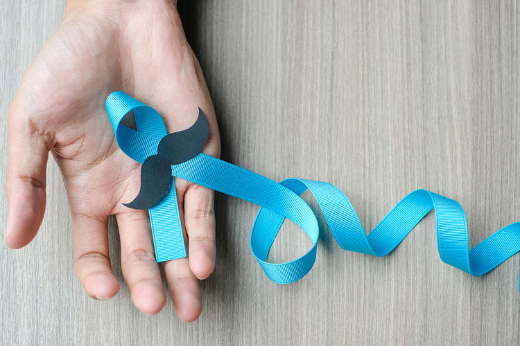 Cropped image of hand holding blue ribbon with mustache on table