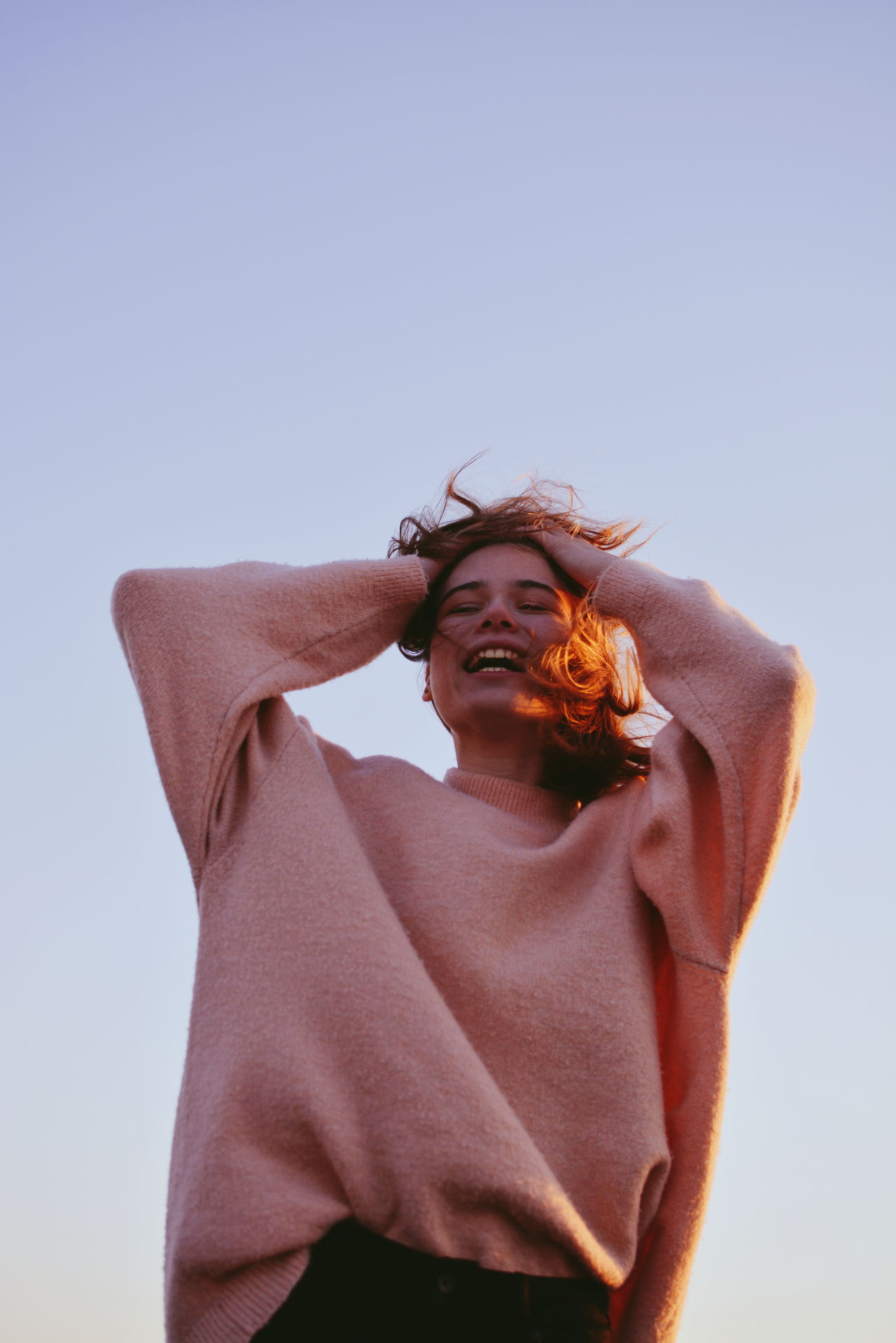Low angle view of smiling teenage girl standing against clear sky