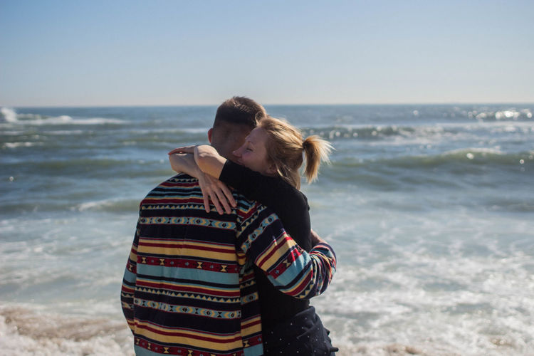 Couple embracing while standing at beach against sky