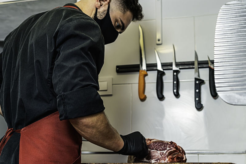 Butcher with mask cutting raw meat in the wood