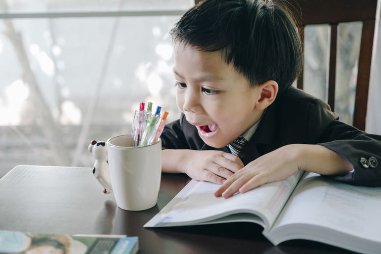 Boy shouting while sitting with book on table