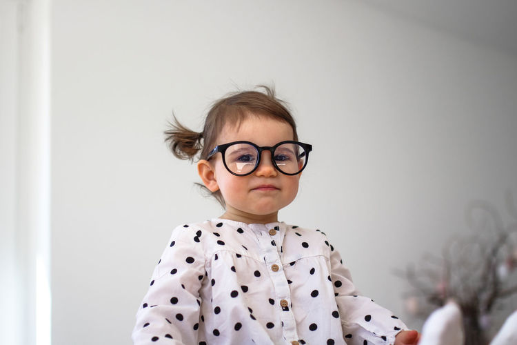A little girl with glasses sits on a wooden table. funny girl 