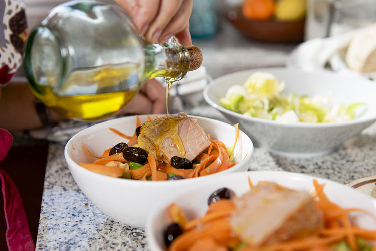 Close up of hand pouring olive oil over a salad with olives and