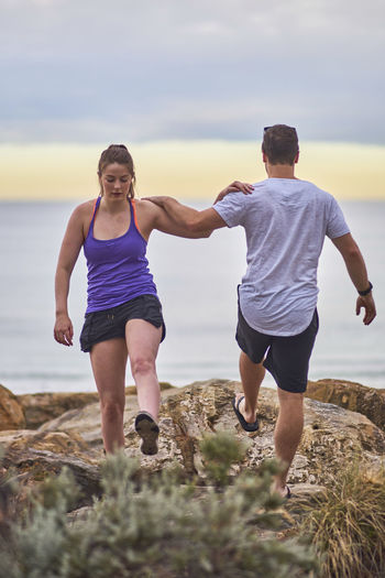 Young woman exercising with fitness instructor at beach