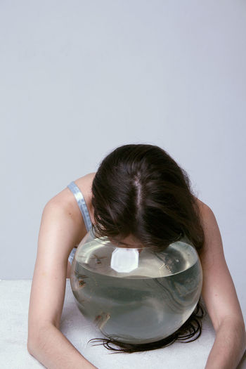 Woman with fish bowl on table against white background