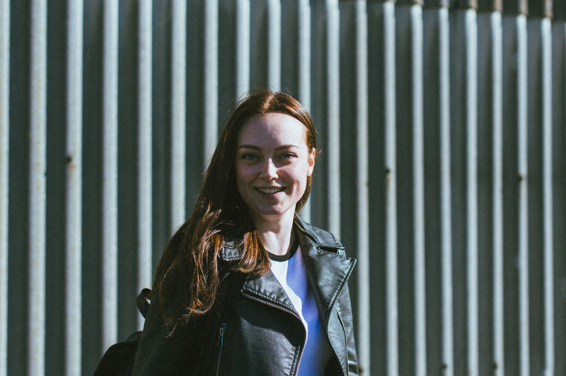 Portrait of smiling young woman standing against metal wall