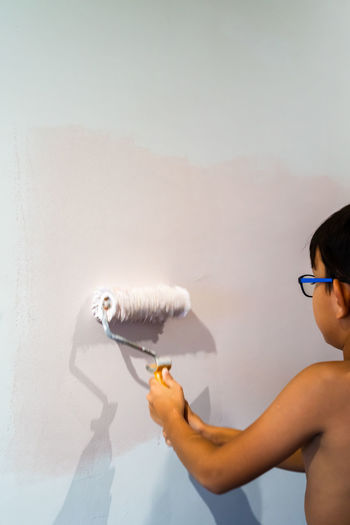 Repair in the apartment. happy child shirtless asian boy paints the wall with pastel pink paint.