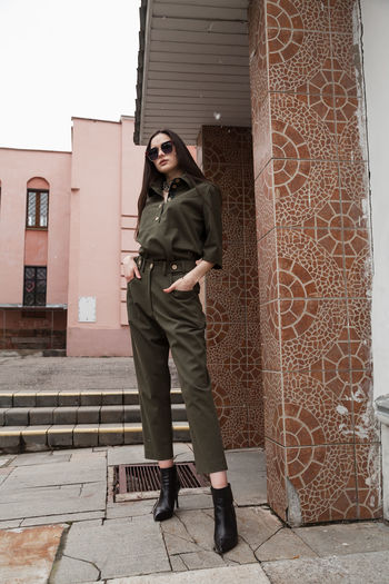 Full length front view portrait of tall slim brunette in green suit in urban setting, fashion  