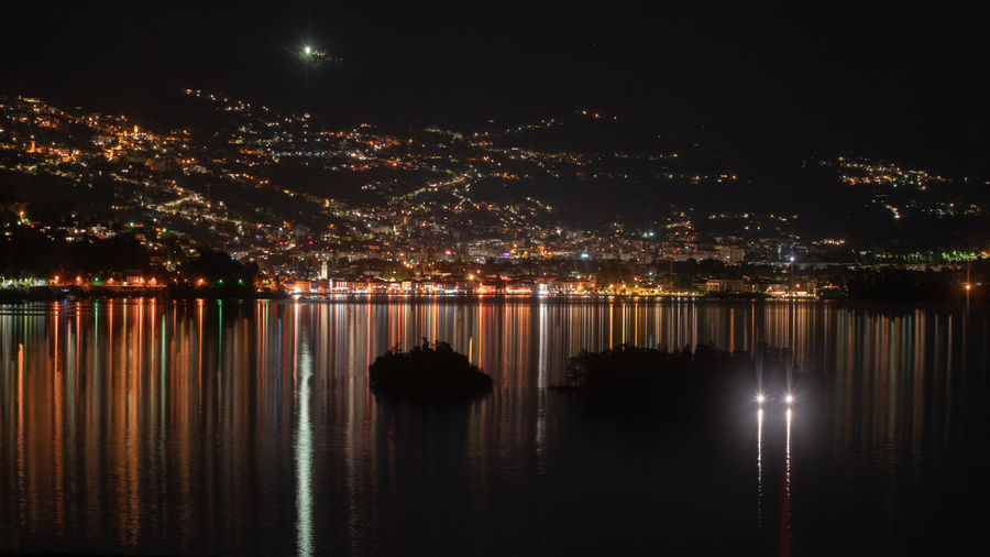 Illuminated city by lake against sky at night