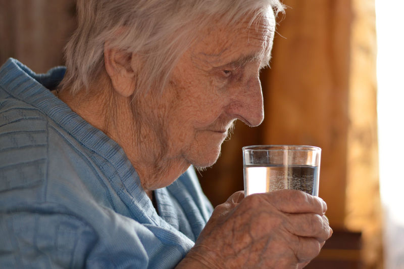 Eldery woman who drinks water from a glass. loneliness, stress, missing grandchildren. 