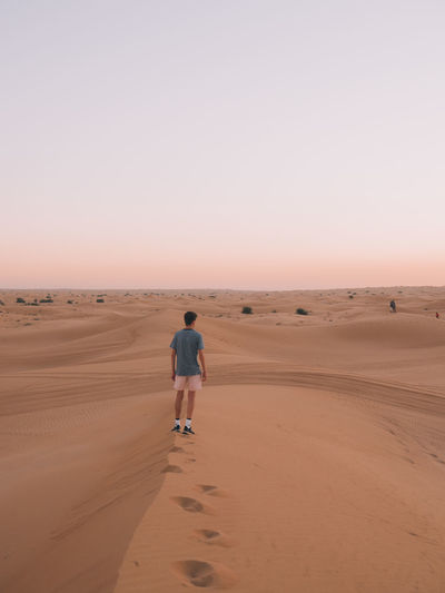 Rear view of man walking on sand in desert against sky