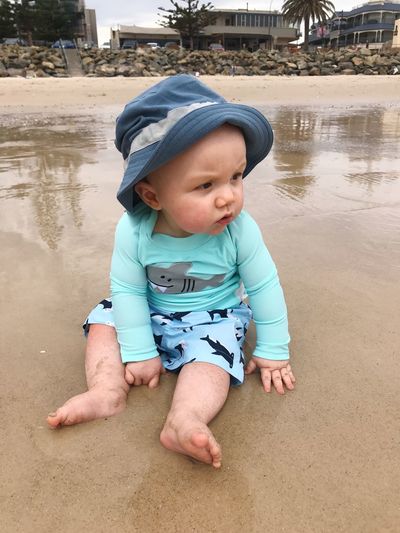 Cute baby boy looking away while sitting at beach