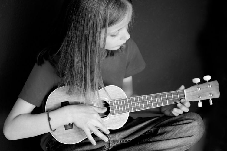High angle view of girl sitting and playing ukelele