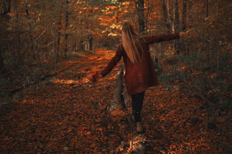 Woman walking on fallen tree in forest during autumn