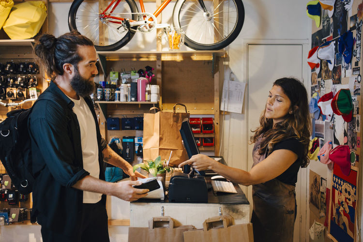 Male customer doing contactless payment to female owner in retail shop