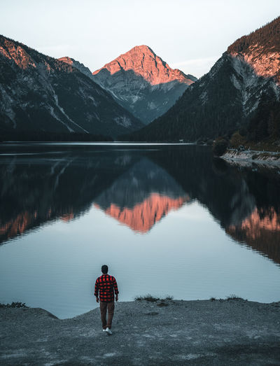 Rear view of man standing on lake against mountain