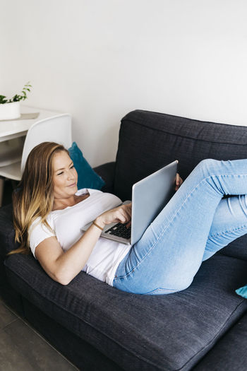 Young woman using laptop while lying on sofa at home
