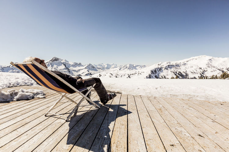 Austria, damuels, senior man relaxing in deckchair on sun deck in winter landscape