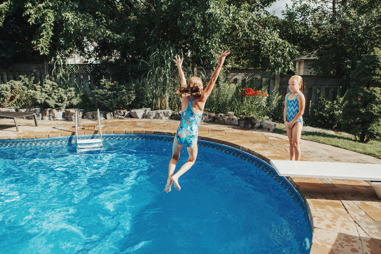 Girl jumping in swimming pool against trees