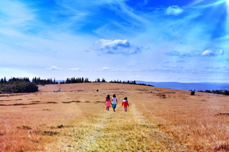 Rear view of girls walking on field against sky