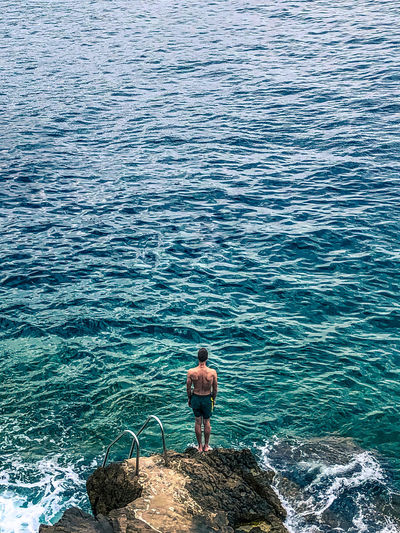 High angle view of man standing on rock by sea