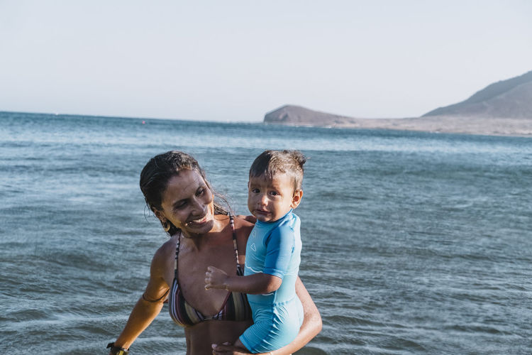 A smiley mother holds her son at the beach