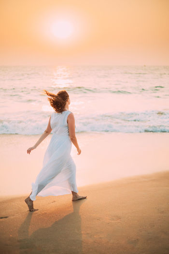 Goa, india. young caucasian woman with fluttering hair in wind in white dress  along seashore sunset 