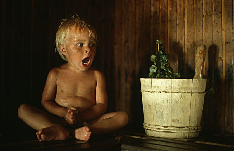 Scared boy looking away while sitting by potted plant against wall