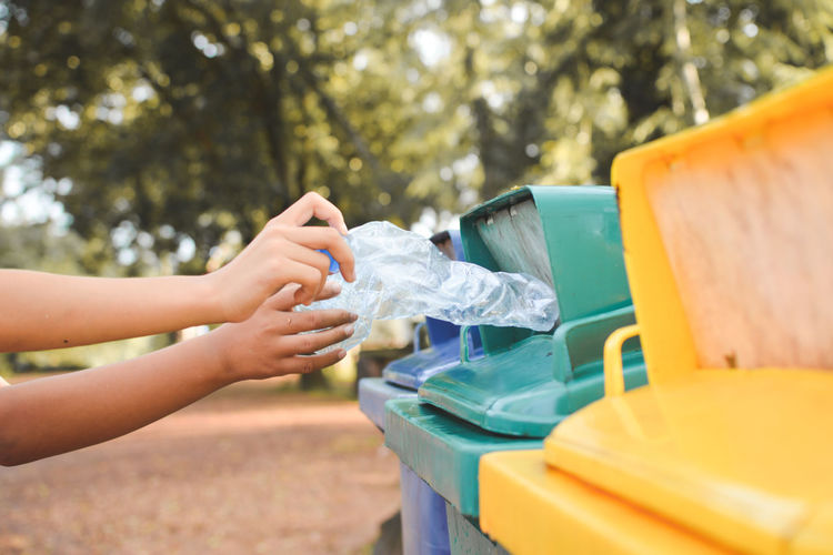 Cropped image of hands throwing crushed bottles in recycling bin