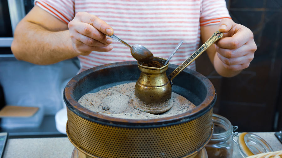 A man brews a turkish coffee traditional way on the sand in the pot called ibrik or cezve.