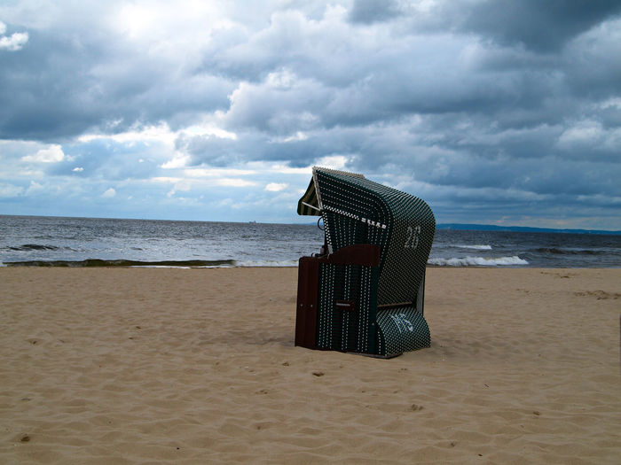 Hooded beach chair on sand overlooking beach against cloudy sky