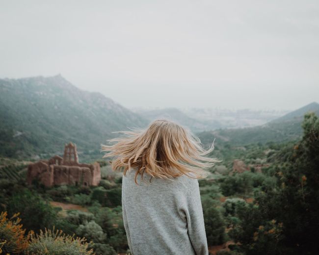 Rear view of woman tossing hair while looking at mountains against sky