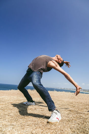 Full length of woman exercising on field against clear blue sky