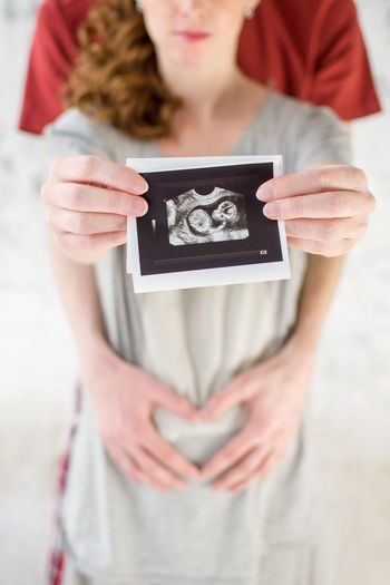 Midsection of pregnant woman holding instant print transfer while standing with man
