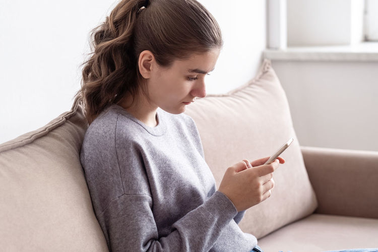 Side view of woman using mobile phone while sitting on sofa at home
