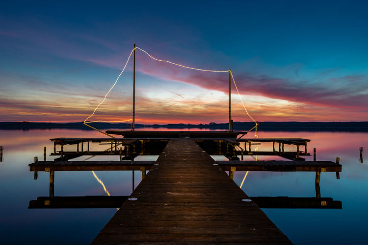 Sailboat moored at pier over lake against sky during sunset
