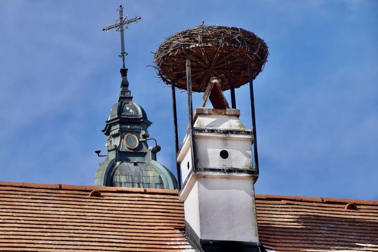Low angle view of traditional church tower with rooftop and stork nest against blue sky
