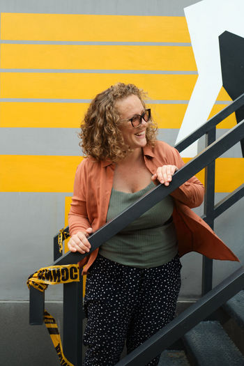 Woman looking away while standing against yellow wall
