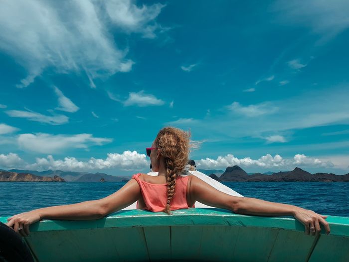 Rear view of woman sitting on boat in sea against blue sky