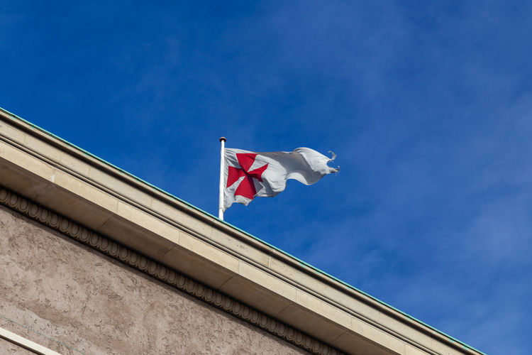 Low angle view of flag against building against blue sky