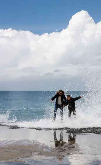 Mother and son wading in sea against cloudy sky