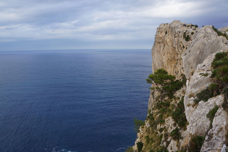 Scenic view of cliff by sea against cloudy sky