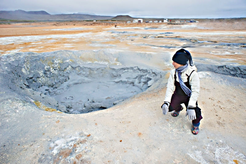 Woman traveling in hverir geothermal area in iceland, boiling volcano mud pots alternative energy
