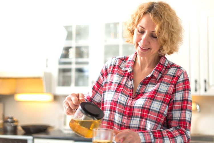 Mature woman pouring tea in cup at kitchen