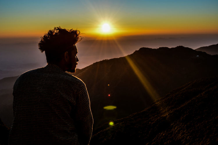 Rear view of man on mountain against sky during sunset