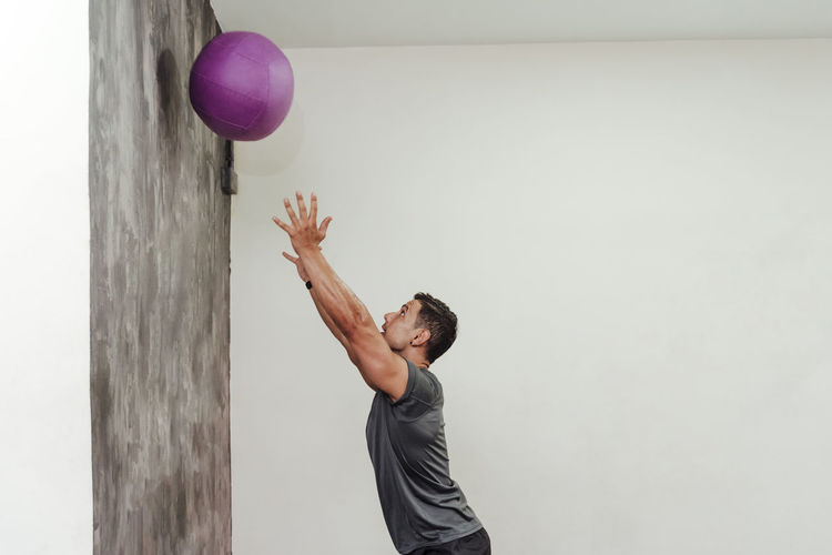 Side view of young man playing with ball against wall