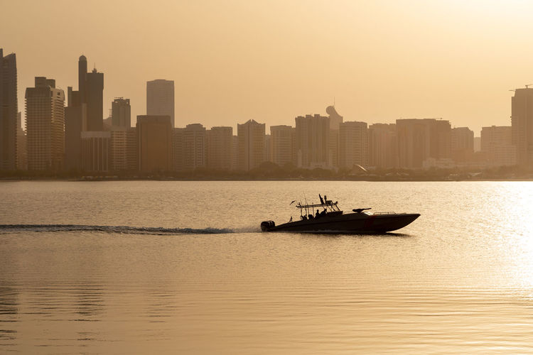 Abu dhabi skyline at sunrise with silhouette of the boat passing through. establishing shot.