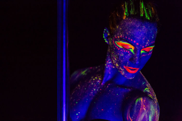 Woman wearing neon clothing by pole against black background