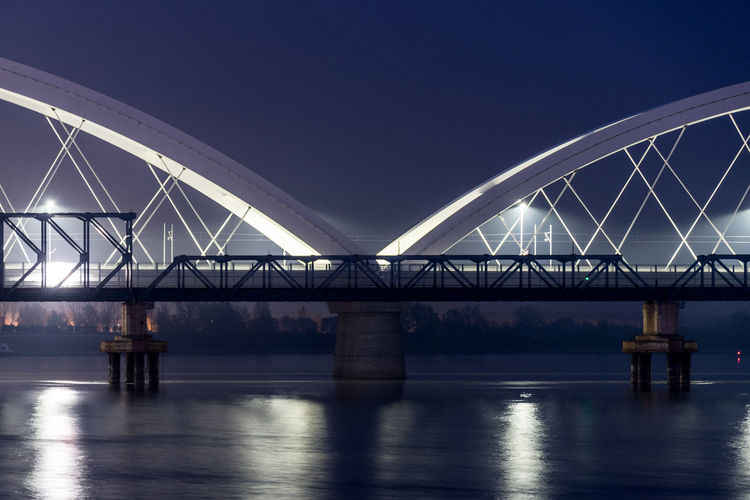 Illuminated bridge over river against clear sky at night